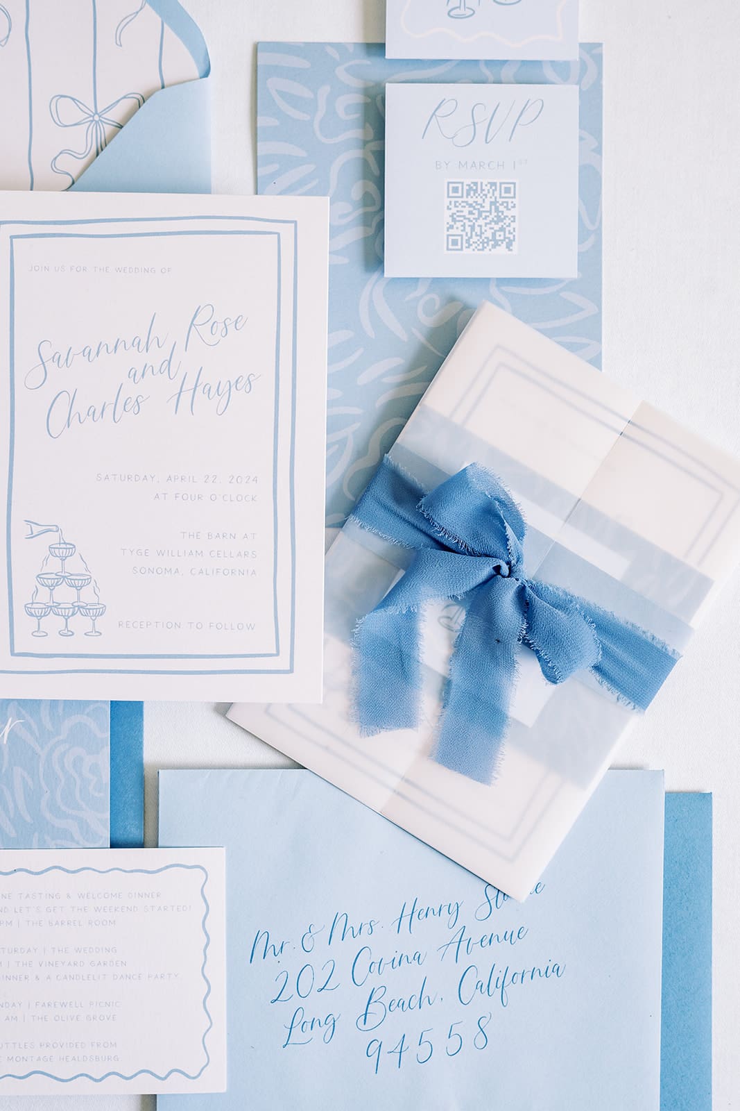 Flatlay of a blue wedding invitation suite with matching ribbon, envelopes, and calligraphy details styled on a soft background.