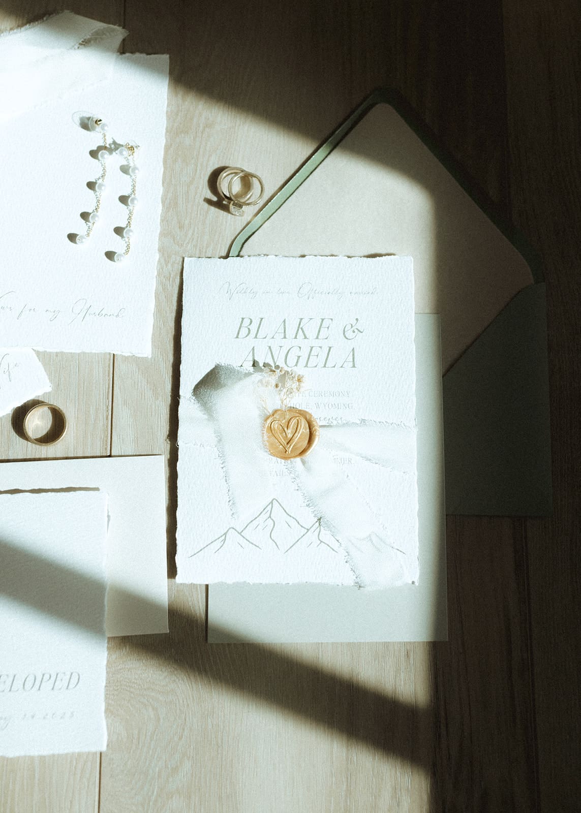 Modern flatlay of custom wedding invitation suite with wax seal, gold accents, and shadow play by a window