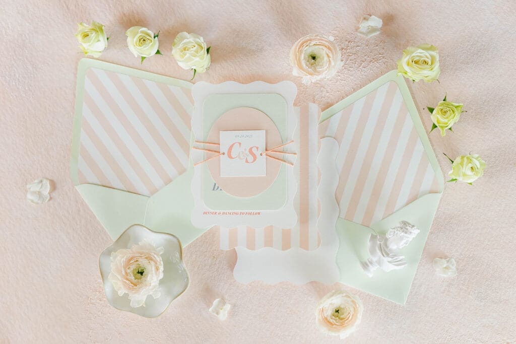 Flatlay of a pastel wedding invitation suite with layered cards, modern typography, and soft blush and green tones for a luxury wine country wedding.