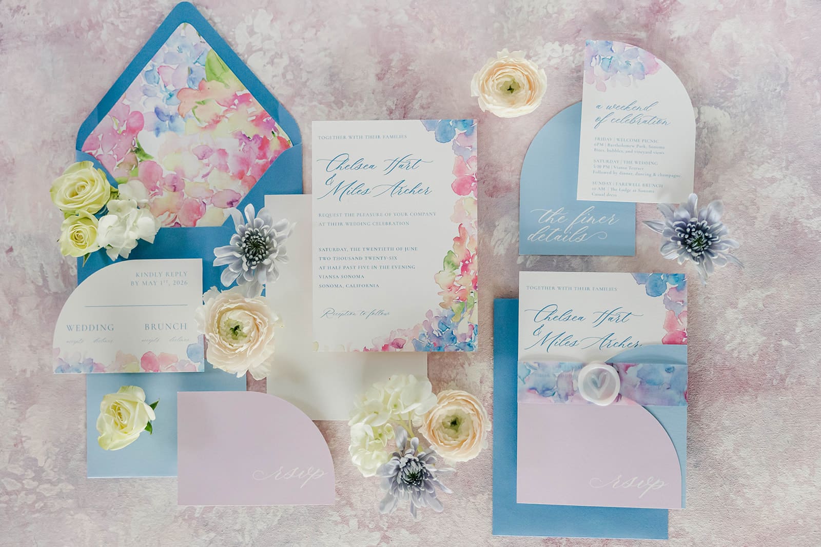 Watercolor wedding invitations with pastel floral design, arched RSVP cards, and blue envelope flat lay.