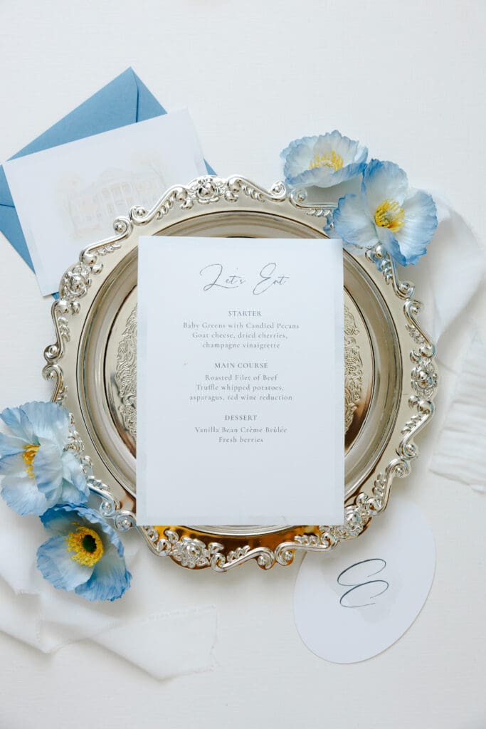 Custom wedding menu on an ornate silver place setting with blue floral details